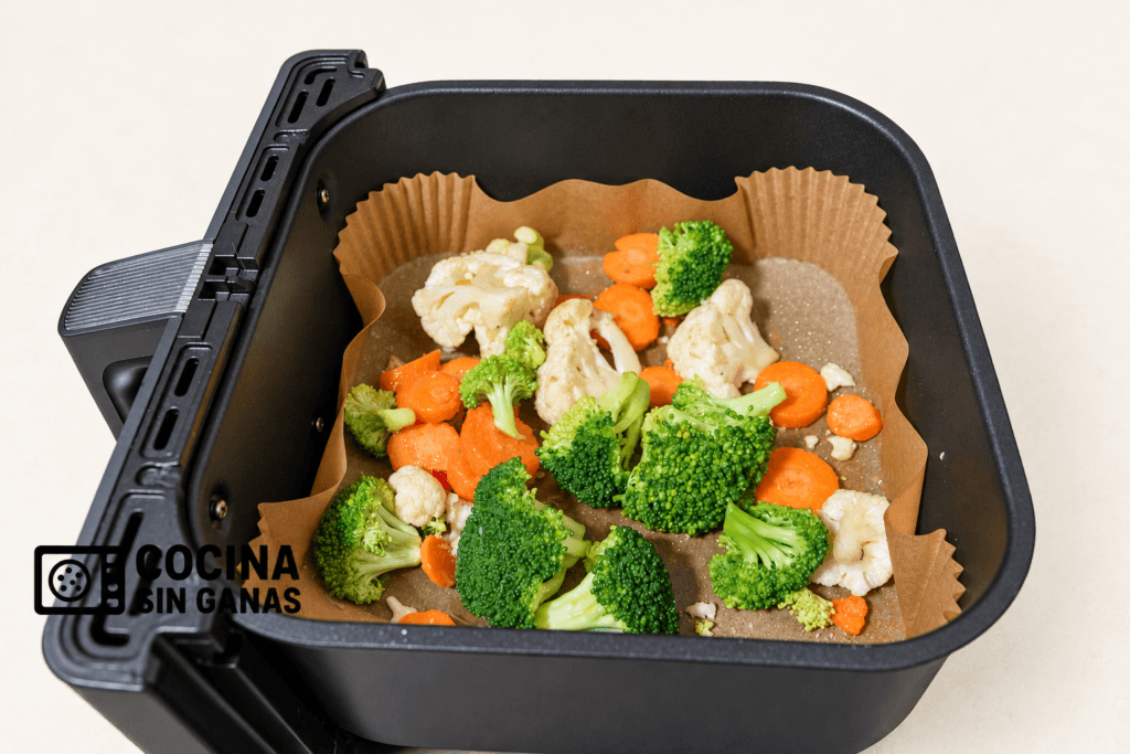 Brócoli, coliflor y zanahoria en la cesta de la freidora de aire con papel de horno